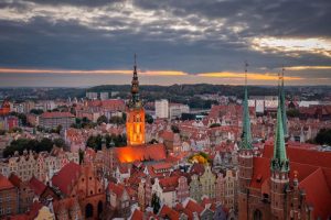 A view of the city with the towering town hall tower, surrounded by historic buildings with red roofs, under a cloudy sky with the warm colors of the setting sun..