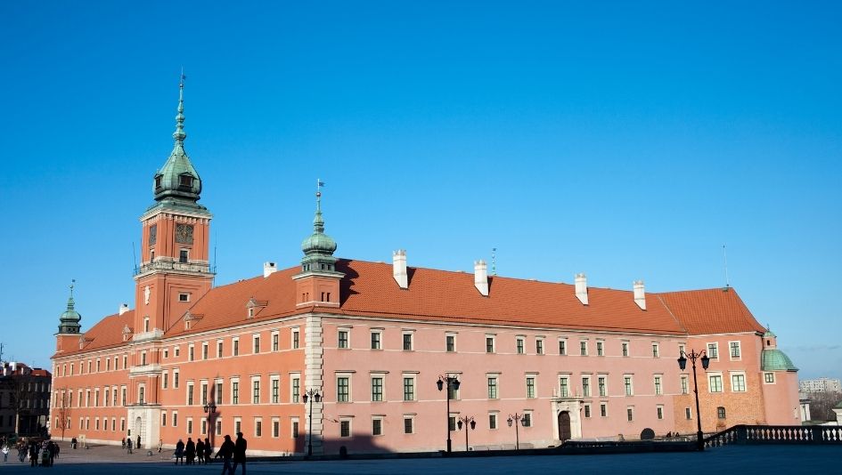 Zamek Królewski w Warszawie z czerwoną dachówką i zielonymi wieżami, na tle błękitnego nieba.