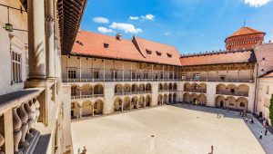 The courtyard of the Royal Castle at Wawel with Renaissance arcades and red roof tiles, against a blue sky.