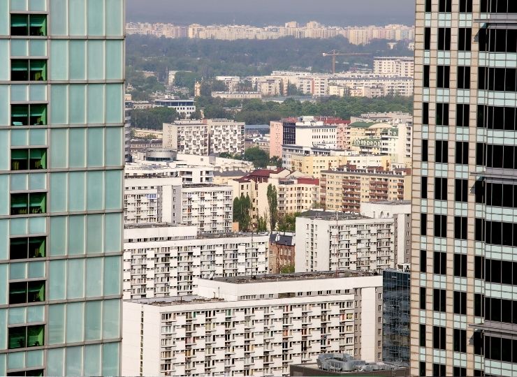 Cityscape featuring multi-story residential and office buildings, with green spaces visible in the background.