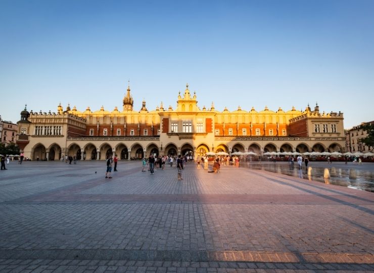 Sukiennice w Krakowie o zachodzie słońca, z ludźmi spacerującymi po Rynku Głównym.