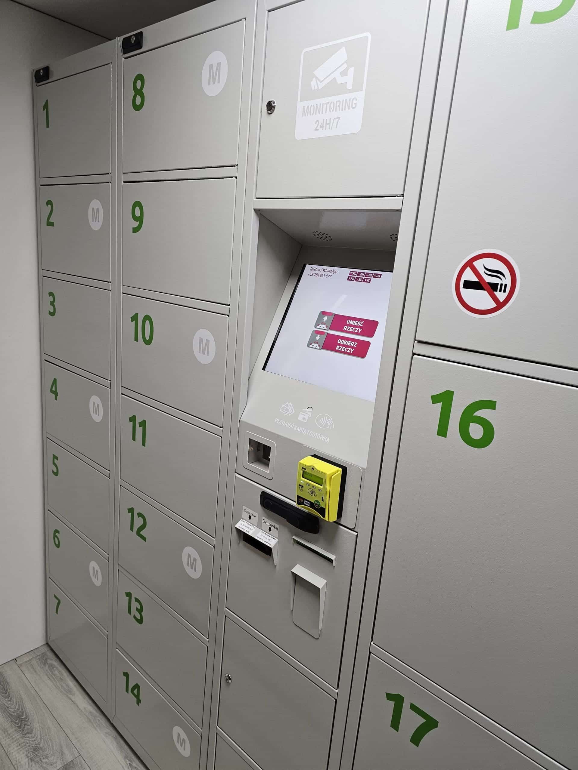 Ряд пронумерованих сірих камер схову із зеленими номерами слугує для зберігання багажу, обладнаний електронною панеллю керування з екраном та картрідером; з правого боку видно знак заборони паління.